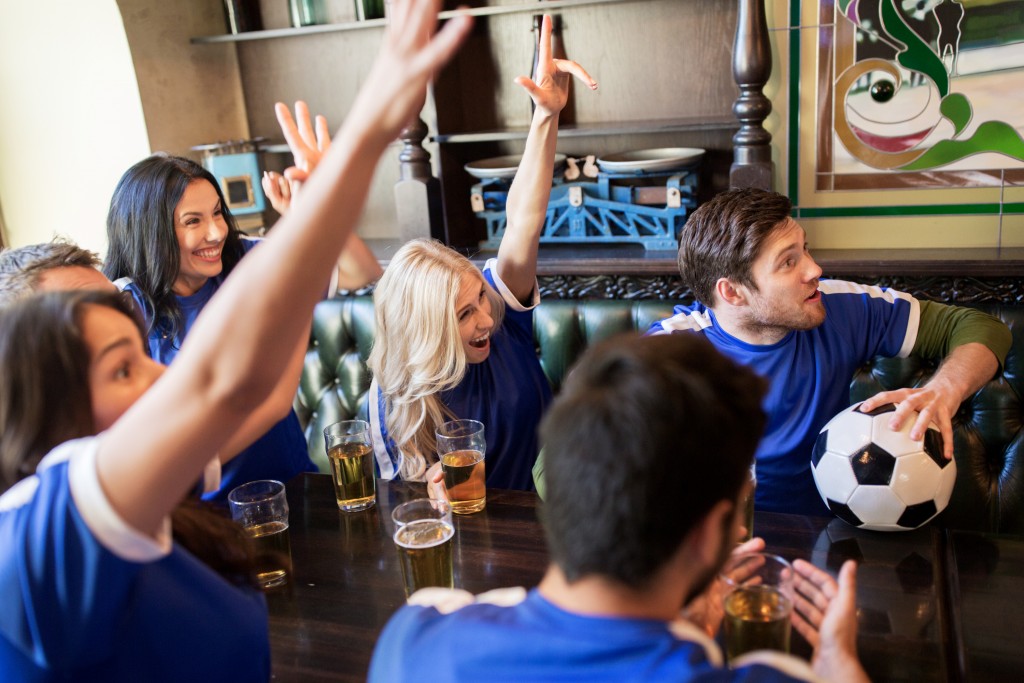 people, leisure and sport concept - happy friends or football fans drinking beer and watching soccer game or match at bar or pub