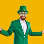 A man dressed in a green St. Patrick's Day themed suit smiling and posing in front of a bright yellow background.