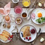 A breakfast spread with a bunny egg holder, toast, berries, nuts, crepe with jam, radishes, a sunny-side-up egg, and orange juice.